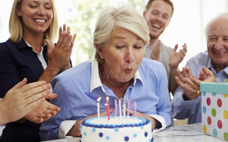 senior-woman-blows-out-birthday-cake-candles-family-party-76286512.jpg