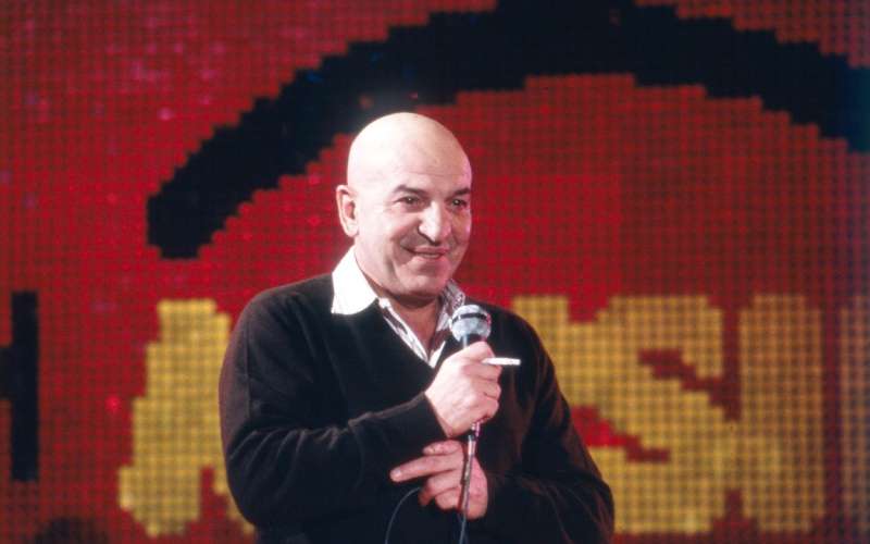 Telly Savalas v svoji najbolj prepoznavni formi - brez las, z mikrofonom in obvezno cigareto v roki.