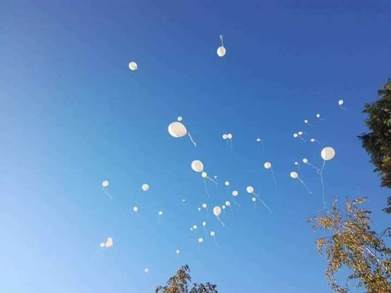 Simboličen spust belih balonov in sporočil v nebo.