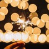 crop-hand-holding-sparkler-near-lights