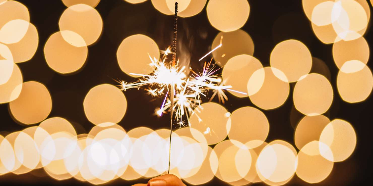 crop-hand-holding-sparkler-near-lights