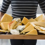 mid-section-woman-holding-cheese-slices-wooden-tray