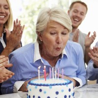 senior-woman-blows-out-birthday-cake-candles-family-party-76286512