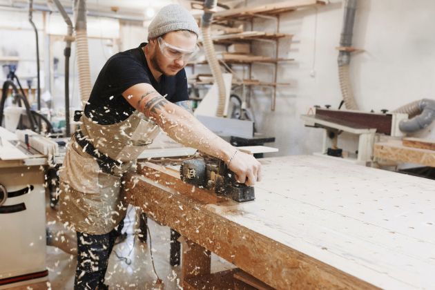 Carpenter working with electric planer on wooden plank in workshop..jpeg