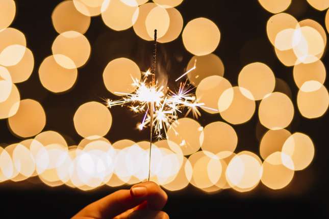 crop-hand-holding-sparkler-near-lights