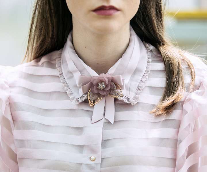 Detajl z broško na ovratniku bluze v rožnatih barvah