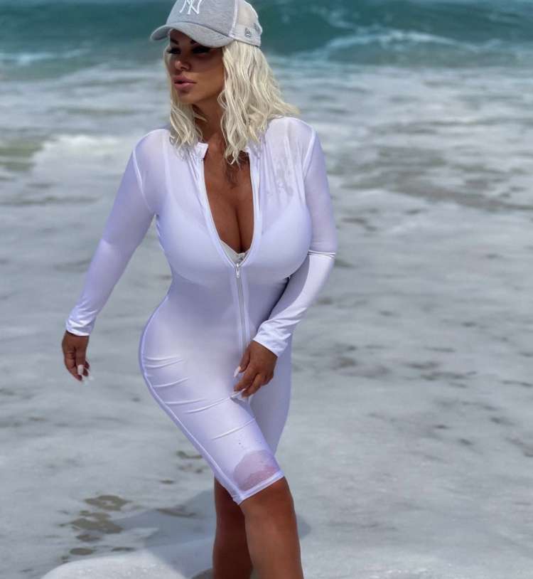 Našobljena, oblečena v bel kombinezon na peščeni plaži ...