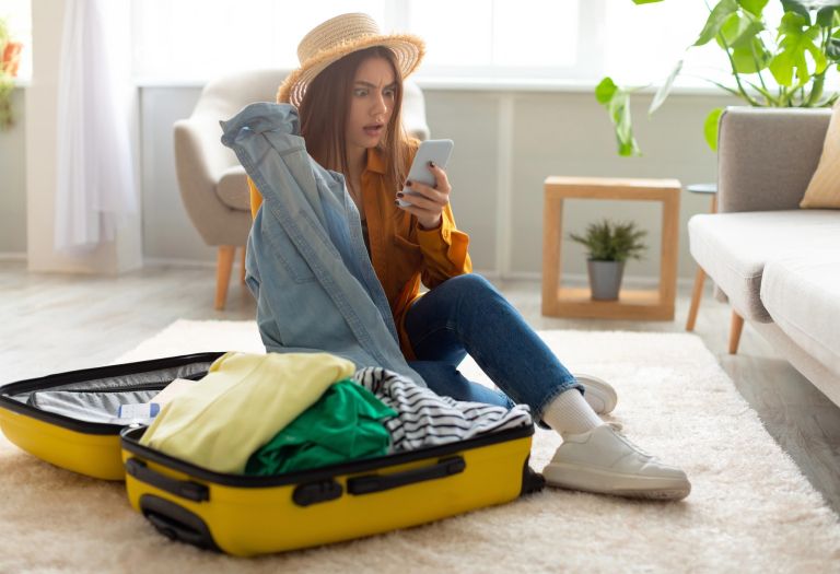 ženska pakira kovček in gleda telefon