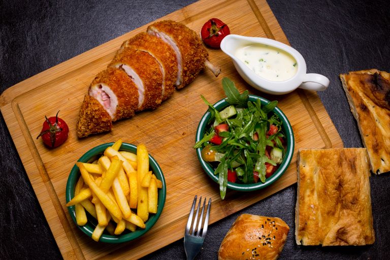 kiev-style-cutlet-wooden-board-with-french-fries-arugula-tomato-cucumber-sauce-top-view.jpg