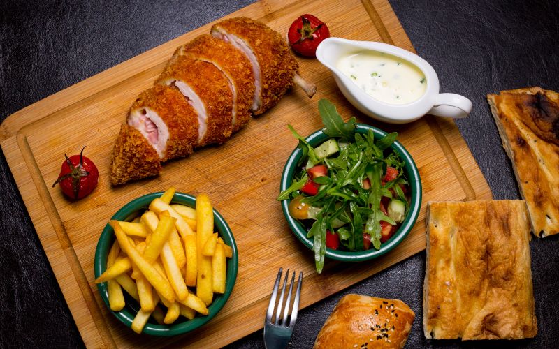 kiev-style-cutlet-wooden-board-with-french-fries-arugula-tomato-cucumber-sauce-top-view.jpg